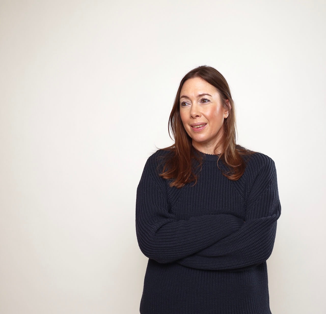 It's actually her. Vikki Ross, founder of Copywriters Unite and all sorts of good things stands to the right of our screen, looking left. She's a white woman with long chestnut brown hair. She's standing with her arms folded, wearing an inky blue jumper and smiling.