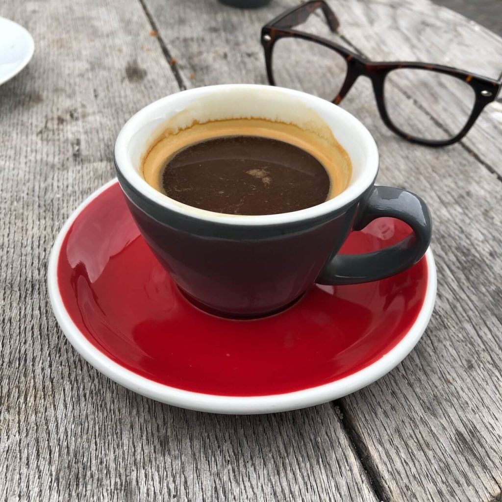 A red cup of coffee on an outside table with a pair of glasses