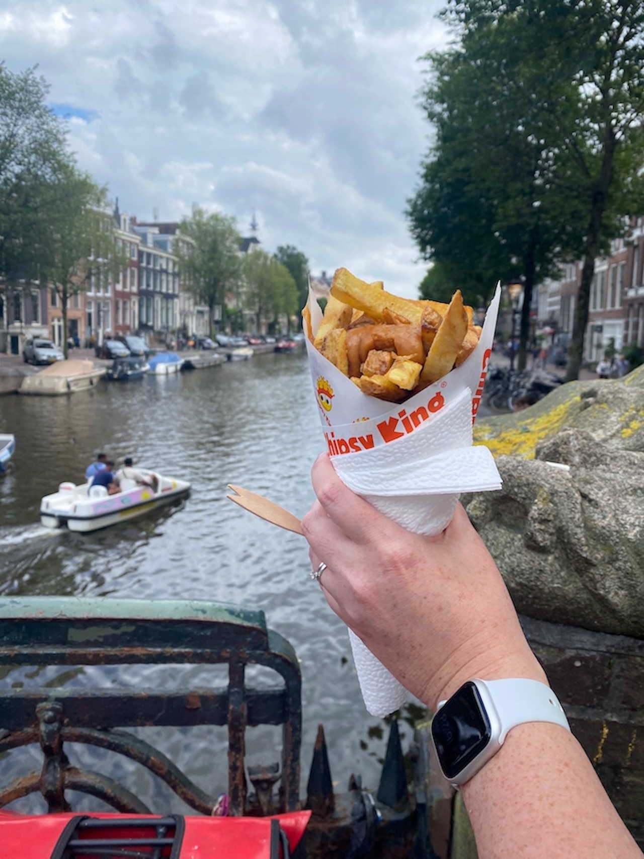 Oh, they were so good. A hand holds a cone of peanut sauce-slathered fat chips aloft over the background of an Amsterdam canal. 